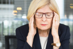 Staršia žena s okuliarmi a blond vlasmi si masíruje spánky pre bolesť hlavy.